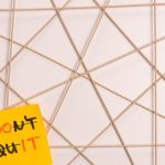 Bright yellow sticky note with motivational message on an abstract geometric design background.