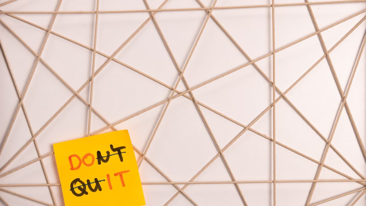 Bright yellow sticky note with motivational message on an abstract geometric design background.